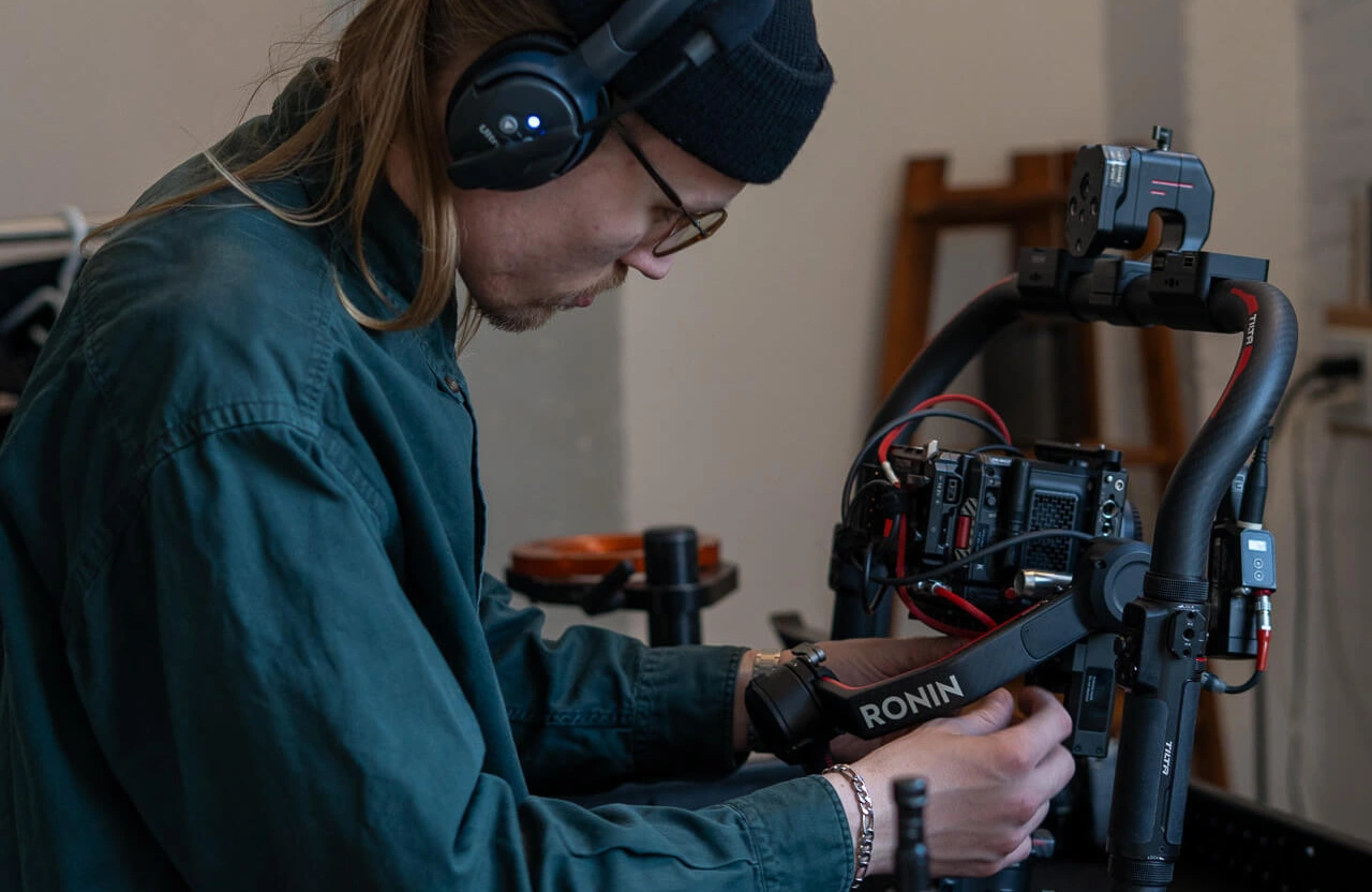 FX Productions Canada A person wearing headphones adjusts a professional camera rig labeled "RONIN" on a table, focused on technical setup. Toronto Video Production Company