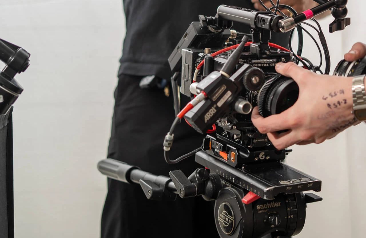 FX Productions Canada A person adjusts the lens on a professional video camera mounted on a tripod, with cables and equipment visible. Toronto Video Production Company