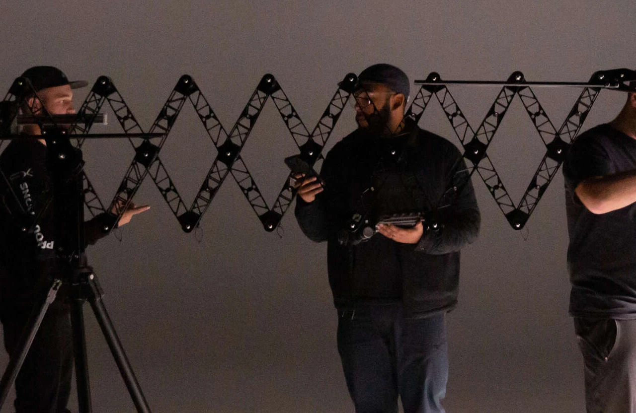 FX Productions Canada Three people stand in front of a large, expandable scissor-like structure, holding electronic devices and wearing dark clothing in a dimly lit room. Toronto Video Production Company