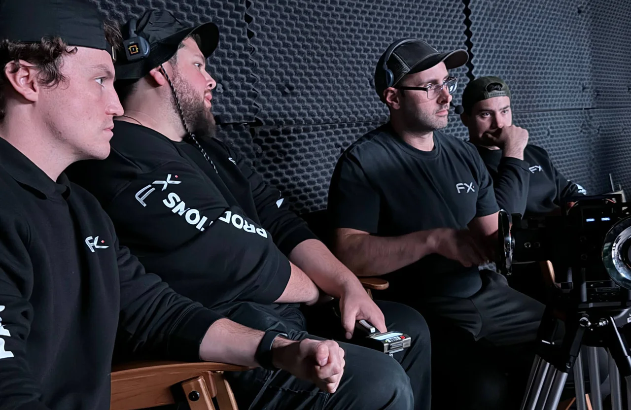 FX Productions Canada Four men wearing black FX shirts and caps sit in a soundproofed room, focused on operating camera equipment. Toronto Video Production Company