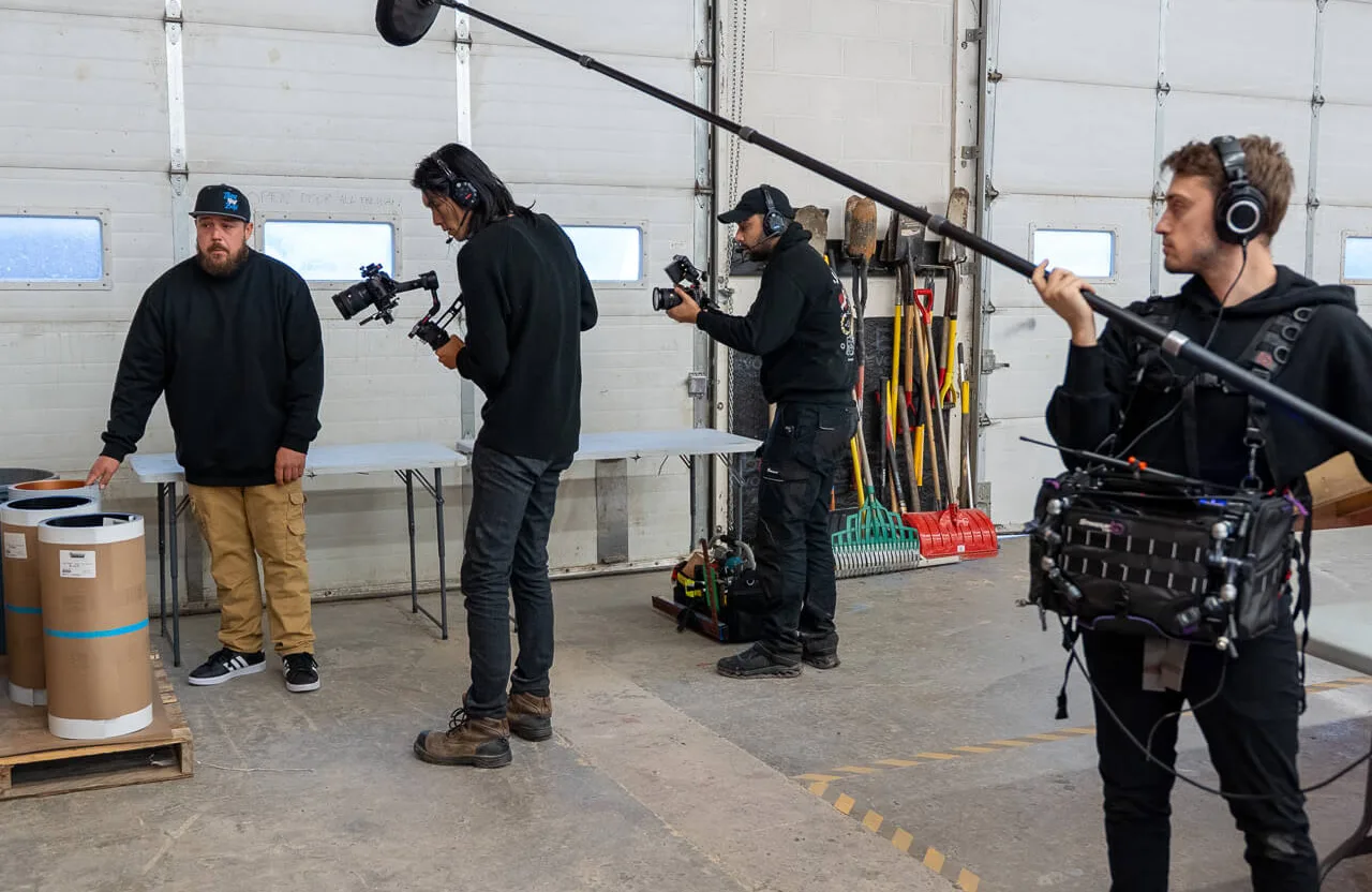 FX Productions Canada Four crew members film and record audio in an industrial garage, equipped with cameras, microphones, and audio gear; various tools are visible in the background. Toronto Video Production Company